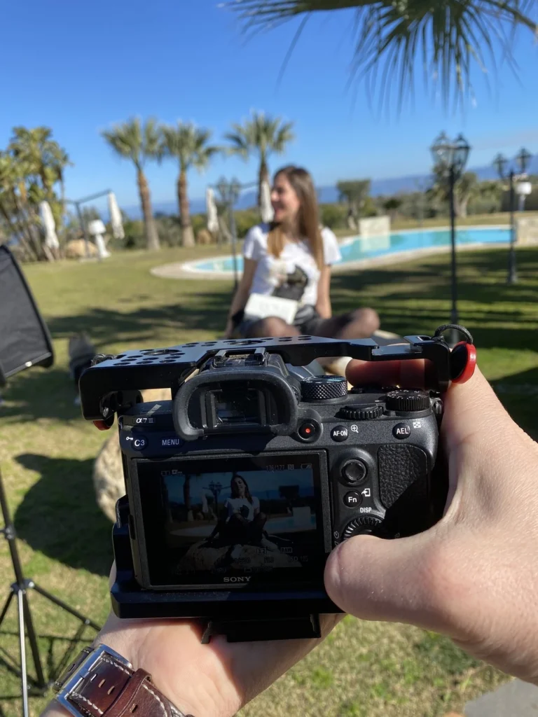 Una fotocamera Sony con gabbia in primo piano durante le riprese di una ragazza seduta in un giardino con piscina